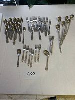 Full view of all cutlery pieces arranged by type on a surface showing spoons, forks, mini forks, pickle forks, and long spoons.