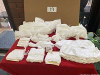 Photo showing 11 pieces of white Swiss lace trim, various patterns and widths, folded and arranged on a red cloth surface against a brown backdrop with number 19.