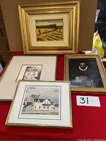 Photo showing four framed art pieces including a painting of workers in a field, a black and white lithograph of a building, a classical portrait, and a modern house print.