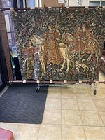 Full view of one large tapestry panel depicting two women on horses and a man holding the horse's rein, richly detailed with floral patterns in the background.