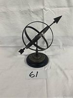 Photo of metal armillary sphere garden sculpture showing intersecting rings and arrow on base.