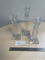 Set of three clear glass candle holders of varying heights arranged on a table.