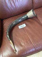 Curved decorative horn with a silver metal cap on one end and a brass/gold-toned tip on the other placed on a brown leather surface.