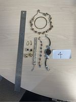 Photo showing the entire jewelry collection with 4 bracelets, 3 pairs of earrings, and 1 necklace placed on a table next to a ruler as size reference.