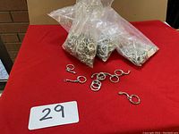 Three clear plastic bags filled with over 100 small silver metal key chain holders, with some loose key holders placed on red fabric surface.