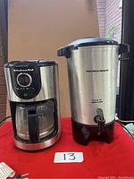 Photo showing KitchenAid drip coffee maker with glass carafe on the left and Hamilton Beach stainless steel percolator with spout on the right, both placed on table.