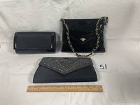 Three ladies evening handbags shown laid on white cloth with ruler for size reference. Includes a rectangular black patent leather clutch, a black patent leather shoulder bag with gold-tone chain strap, and a black fabric clutch with silver bead decoration.