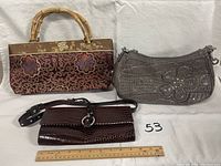 Photo showing three ladies handbags including maroon/gold patterned fabric bag with bamboo handles, gray Guess faux crocodile bag with floral detail, and dark brown faux crocodile clutch.