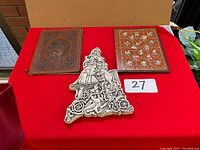 Two leather book covers and one ornate old printing block placed on a red cloth background