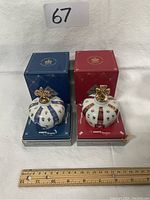 Two mini porcelain cognac decanters shaped as crowns, one blue and one red, presented on their matching boxes with ruler for size reference.