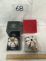 Two mini porcelain cognac decanters with their original boxes. The decanter on the left is decorated with green and gold ribbons and topped with a gold crown. The decanter on the right has red and gold ribbons with heraldic symbols and a cork stopper with a golden cross.