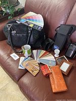 Wide shot of all items in the lot on a brown leather couch, showing paint sample cards, handbags, wallets, and small decorative items including an egg cup and mug.