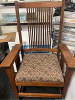 Front view of the wooden chair showing the slatted back and armrests.
