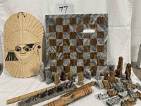 Shows onyx chessboard with chess pieces set up, large carved wooden mask positioned behind, wooden percussion instrument and wooden elephant figurines in front with a ruler for scale.