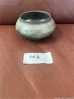 Front view of handcrafted Raku pottery bowl on brown leather surface with lot number 102 indicated on paper