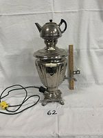 Photo of the metal samovar with teapot on a white cloth background showing the full height with an electric cord and plug visible.