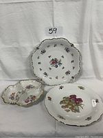 Three porcelain serving dishes with floral decorations and gold trim arranged on white fabric background.