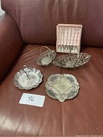 Five silver metal filigree baskets and boxed set of six silver spoons arranged on brown leather couch