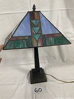 Full view of the Tiffany style table lamp with stained glass shade showing geometric patterns in blue, purple, green, and amber glass with a dark metal base.