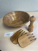 Wooden salad bowl with two wooden salad scoop servers and a wooden pepper mill on a table from top and side angles showing the bowl's wide rim and scoop prongs.