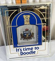 Front view of rectangular wall clock with chrome mirrored frame and Boodle Dry Gin bottle design at center with clock hands on label. Text below says 'It's time to Boodle'.