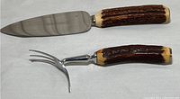 Photo of serrated knife and 3-pronged fork with antler horn handles on white background.