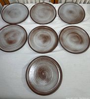 Seven vintage stoneware pottery plates arranged in two rows on white cloth, showing circular designs and uniform size.