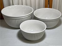 Three white ceramic nesting mixing bowls arranged side by side showing sizes and ribbed exterior