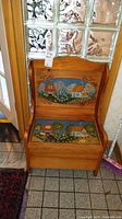 Front view of pine storage bench with painted village scene on inside of seat lid and seat top.