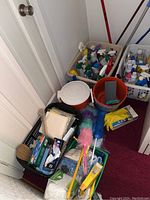 Four bins filled with various cleaning supplies and tools along with loose items like feather dusters and gloves on the floor.