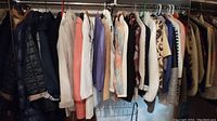 Hanging rack with women’s jackets in various colors and patterns, primarily light and neutral tones with a few darker pieces, including a black quilted jacket.