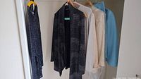Five women's clothing items including jackets and sweaters on hangers of various colors and styles.
