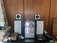 Panasonic SA-PM29 CD stereo system with two speakers, Sony Discman, Sony Walkman, and accessories arranged on a table in front of a wood paneled wall.