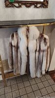Full front view of silver fox fur jacket on hanger under mirror