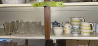 Overall shelf view showing clear glass tumblers on left and ceramic pitchers, bowl, teapot on right
