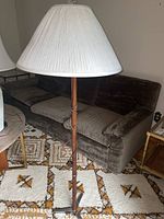 Full view of floor lamp showing wood pole with carved details, metal base, and white pleated lampshade.