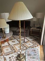 Full view of floor lamp showing brass ornate base and pleated shade placed on a patterned rug in living room.