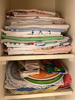 Stack of folded tablecloths and napkins on shelf with assorted colors and textures visible