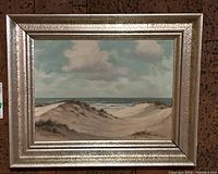 Full view of the framed painting showing the coastal dunes and sky, with detailed textures visible on painting and frame.