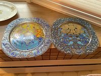 Two 11x11 decorative plates with ornate blue borders and colorful folk art style figures, placed on a windowsill