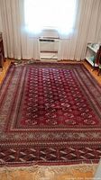 Full view of the rectangular woven rug with intricate multi-layered border patterns and red medallion motifs in center, placed on hardwood floor in a room.