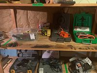 Wide frontal view of shelving holding tools including drill, jigsaw, screwdrivers, stapler, and accessories in plastic bin.