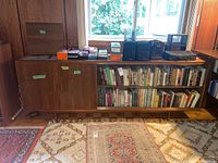 Full view of vintage wood cabinet with items on top and shelves filled with books and miscellaneous items.