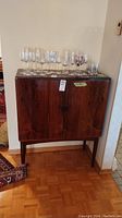 Full frontal view of rosewood bar cabinet showing two doors, tapered legs, and wine glasses on top for scale