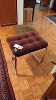 Side angle view of vintage brown tufted upholstered stool with chrome metal base.