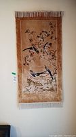 Full view of the beige wall hanging rug with birds and floral design, fringes on top and bottom.
