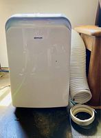 Front view of white Brada portable air conditioner and dehumidifier with vent hose coiled beside it.