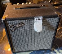 Front view of Fender bass amplifier showing Fender logo, grey grille, black textured case and metal corner protectors.