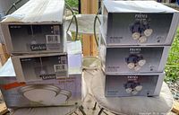 Boxes of 4 Prima ceiling light fixtures MG-C400-3-BZ stacked on right, 2 Levico ceiling light boxes MG-MP-401 stacked on left on outdoor furniture.