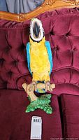 Front view of the FuReal macaw bird figurine perched on its branch base, showing vibrant yellow and blue feathers and facial details.